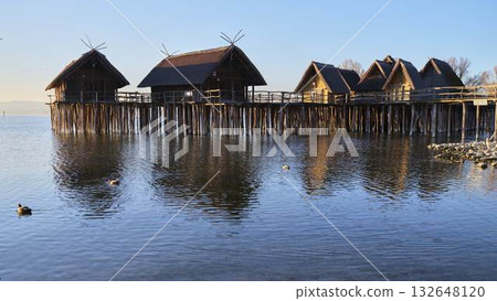 Scenic lakeside wooden houses on stilts reflecting in calm water at sunset 132648120