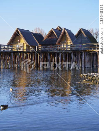 Stilt houses on a tranquil lake at sunset with reflections in calm water Stilt houses on a tranquil lake at sunset with reflections in calm water 132648121