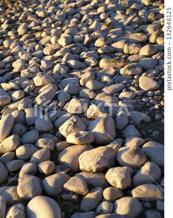 Smooth stones reflect warm sunset light along a serene shoreline near the coast 132648125