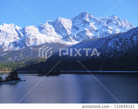 Snow-capped mountains rise majestically over a tranquil lake under a clear blue sky in a winter landscape Snow-capped mountains rise majestically over a tranquil lake under a clear blue sky in a winter landscape 132648181