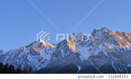 Snow-capped mountains under a clear blue sky at sunrise in a serene alpine landscape 132648183
