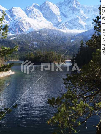 Breathtaking snowy mountain landscape with a serene lake surrounded by evergreen trees in clear weather 132648212