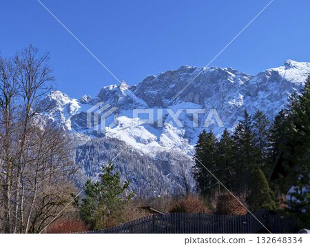Snow-capped mountains rise against a clear blue sky in a serene winter landscape Snow-capped mountains rise against a clear blue sky in a serene winter landscape 132648334