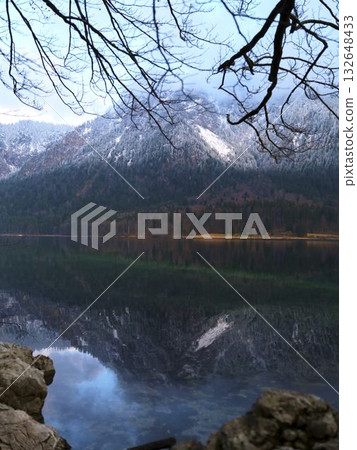 Serene lake reflects snowy mountains under cloudy sky during early morning light 132648433