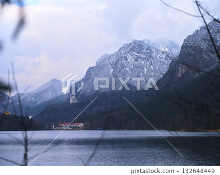 Snow-capped mountains reflect on a tranquil lake near a quaint resort on a chilly winter day 132648449