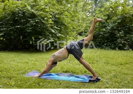 A man is practicing yoga amidst the beauty of nature, specifically in the Downward Dog pose A man is practicing yoga amidst the beauty of nature, specifically in the Downward Dog pose 132649184