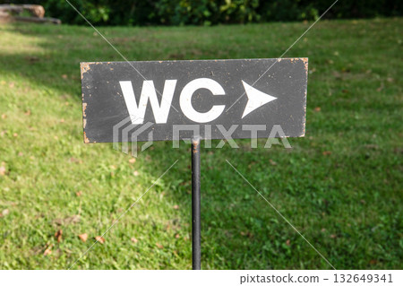 Black WC sign with white letters and arrow pointing direction, mounted on a metal post in grassy Black WC sign with white letters and arrow pointing direction, mounted on a metal post in grassy 132649341
