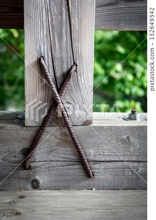 Detailed view of weathered wooden beam reinforced with crossed rusty steel rods Detailed view of weathered wooden beam reinforced with crossed rusty steel rods 132649342