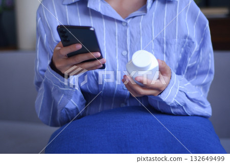 Young Asian women using phone checking on direction how to use vitamin supplementary, medicine before taking it. Young Asian women using phone checking on direction how to use vitamin supplementary, medicine before taking it. 132649499