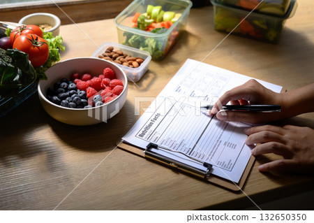 Nutritionist writing a healthy meal plan with fresh fruits, vegetables, and nuts on the table Nutritionist writing a healthy meal plan with fresh fruits, vegetables, and nuts on the table 132650350