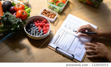 Nutritionist writing a healthy meal plan with fresh fruits, vegetables, and nuts on the table 132650353
