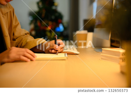 Man writing note while using laptop at table in office Man writing note while using laptop at table in office 132650373