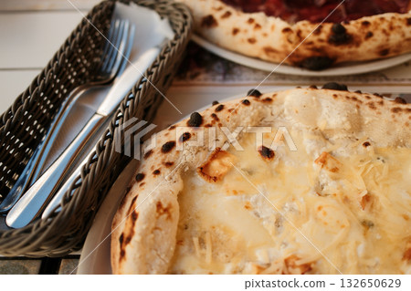 Freshly baked two pizza with golden cheese next to basket of cutlery, ready for perfect dining experience. Italian outdoor cafe, close view Freshly baked two pizza with golden cheese next to basket of cutlery, ready for perfect dining experience. Italian outdoor cafe, close view 132650629
