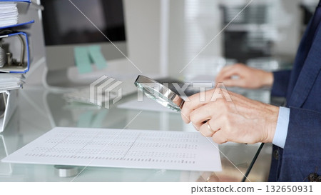 Hand holding magnifying glass, inspecting financial document, performing audit and business analysis. Audit and taxes in business 132650931