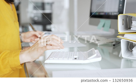 Accountant in yellow blouse working on financial budget, calculating taxes and expenses, managing paperwork in office. Audit and taxes in business 132650936