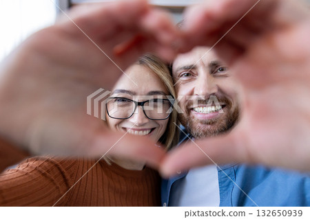 Smiling couple creating a heart with their hands and looking at the camera, conveying love, joy and close connection in a candid, cozy indoor portrait of partners Smiling couple creating a heart with their hands and looking at the camera, conveying love, joy and close connection in a candid, cozy indoor portrait of partners 132650939