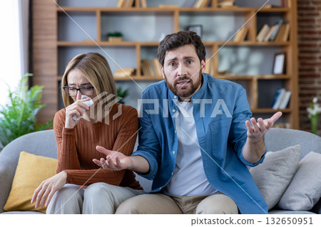 Couple in a tense online therapy session at home, woman crying, man frustrated, discussing relationship problems and seeking professional guidance via video call. 132650951