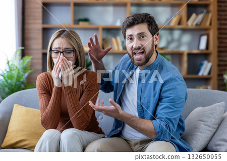 Man shouting and gesturing while woman cries and uses a tissue, both sitting on a couch, representing family conflict, relationship problems, and virtual psychological consultation. Man shouting and gesturing while woman cries and uses a tissue, both sitting on a couch, representing family conflict, relationship problems, and virtual psychological consultation. 132650955