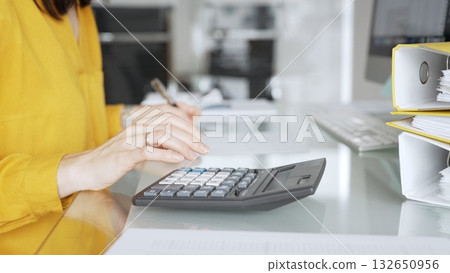 Woman in yellow blouse calculating finances, managing budget, doing taxes, working on accounting documents in office workspace. Audit and taxes in business Woman in yellow blouse calculating finances, managing budget, doing taxes, working on accounting documents in office workspace. Audit and taxes in business 132650956