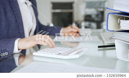 Professional accountant calculating finances and managing paperwork on an office desk, analyzing taxes and budget planning. Audit and taxes in business Professional accountant calculating finances and managing paperwork on an office desk, analyzing taxes and budget planning. Audit and taxes in business 132650964