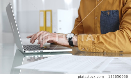 Professional working on laptop, typing at office desk, managing documents and business tasks. Audit and taxes in business 132650966