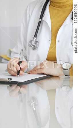 Female physician or medic completing paperwork, preparing a diagnosis, or providing healthcare service in a clean modern office. Medicine, healthcare and science concept 132650998