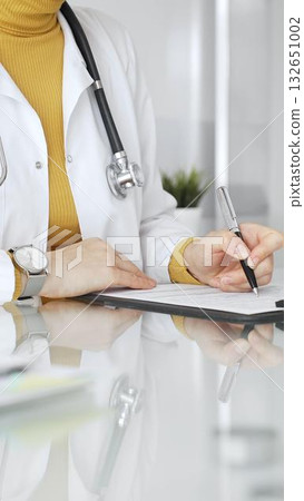 Female physician or medic completing paperwork, preparing a diagnosis, or providing healthcare service in a clean modern office. Medicine, healthcare and science concept 132651002