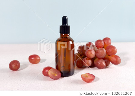 Grape seed oil in dropper bottle with fresh green grapes on a blue background. Skin care concept. Grape seed oil in dropper bottle with fresh green grapes on a blue background. Skin care concept. 132651207