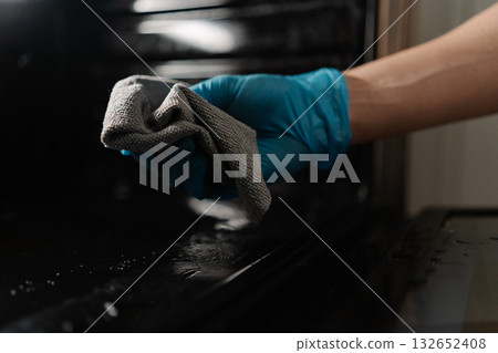 Cleaning company worker in rubber gloves cleaning inside of oven with gray rag, ensuring hygiene and cleanliness in kitchen, closeup. Concept of domestic work, housekeeping and household. Cleaning company worker in rubber gloves cleaning inside of oven with gray rag, ensuring hygiene and cleanliness in kitchen, closeup. Concept of domestic work, housekeeping and household. 132652408