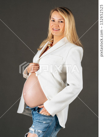 Studio image of expecting mother in white jacket and jeans, side pose, peaceful and confident maternity look Studio image of expecting mother in white jacket and jeans, side pose, peaceful and confident maternity look 132652525