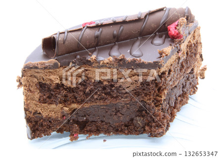 Close-up of a slice of a multi-layered chocolate cake. The layers of dark sponge cake and chocolate cream mousse are clearly visible. The dessert is decorated with chocolate icing, a curl. Close-up of a slice of a multi-layered chocolate cake. The layers of dark sponge cake and chocolate cream mousse are clearly visible. The dessert is decorated with chocolate icing, a curl. 132653347