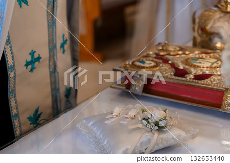 Ornate Wedding Ring Pillow with White Flowers and Gold-Embellished Religious Book on Church Altar 132653440