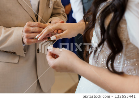 Close-up of a groom placing a wedding ring on his bride's finger during a heartfelt ceremony in soft natural light Close-up of a groom placing a wedding ring on his bride's finger during a heartfelt ceremony in soft natural light 132653441