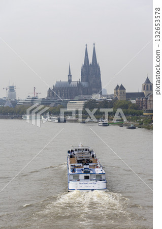 A barge sails along the Rhine towards Cologne Cathedral. 132653578