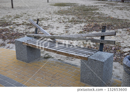 A broken wooden bench stands on a brick path 132653600