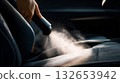 Close-Up of Handheld Vacuum Cleaning Car Seat with Visible Dust Cloud and Fabric Texture 132653942