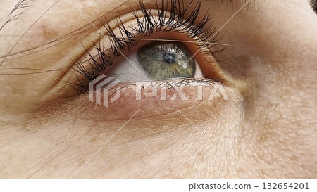 Focus on right green eye of attractive girl blinking and looking up. Portrait of a female pretty face. Calm facial expression of young woman. Tranquil sight of beautiful lady. 132654201