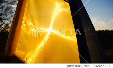 Blue-yellow symbol of Ukraine waving at wind against the background of sunlight. Ukrainian flag illuminated by sun fluttering at countryside. Concept of peace and support against russian aggression Blue-yellow symbol of Ukraine waving at wind against the background of sunlight. Ukrainian flag illuminated by sun fluttering at countryside. Concept of peace and support against russian aggression 132654225