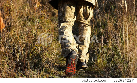 Low view to male feet of ukrainian soldiers going along trail at countryside. Legs of young army man walking through dry grass at sunny day. War in Ukraine. Slow motion 132654227