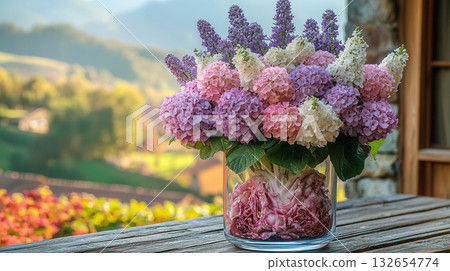 Glass vase with vibrant arrangement of pink and white hydrangea flowers, filled with purple cabbage leaves at bottom, placed outdoors with golden hour light in background. 132654774