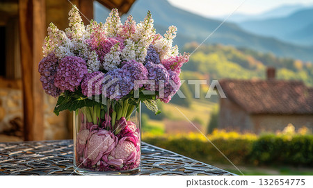 Glass vase with vibrant arrangement of pink and white hydrangea flowers, filled with purple cabbage leaves at bottom, placed outdoors with golden hour light in background. Glass vase with vibrant arrangement of pink and white hydrangea flowers, filled with purple cabbage leaves at bottom, placed outdoors with golden hour light in background. 132654775
