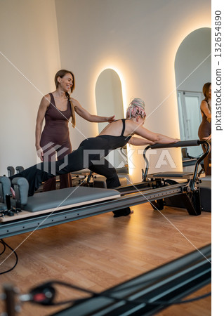 Pilates instructor supports clients, instructor provides supportive guidance for gentle rehabilitation Pilates instructor supports clients, instructor provides supportive guidance for gentle rehabilitation 132654890