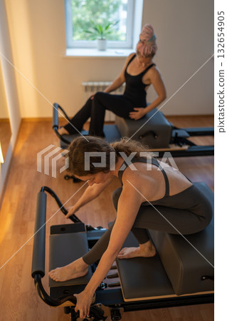 Happy and Tired woman having rest after pilates workout. Tired and exhausted female athlete sitting on reformer bed. 132654905