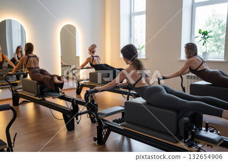 Fitness instructors performing pilates exercises using reformer beds and resistance bands, promoting healthy lifestyle and core strengthening 132654906