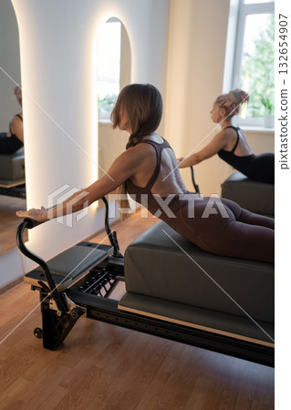 Fitness instructors performing pilates exercises using reformer beds and resistance bands, promoting healthy lifestyle and core strengthening Fitness instructors performing pilates exercises using reformer beds and resistance bands, promoting healthy lifestyle and core strengthening 132654907