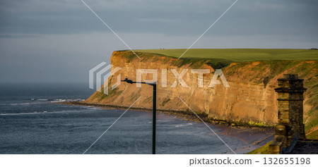 Huntcliff at Saltburn by the Sea reflecting golden light at sunset with a street lamp and chimney in the foreground Huntcliff at Saltburn by the Sea reflecting golden light at sunset with a street lamp and chimney in the foreground 132655198