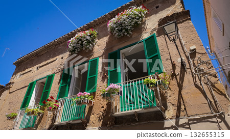 Green window shutters and colorful flowers decorating building facade in Tropea, Italy 132655315