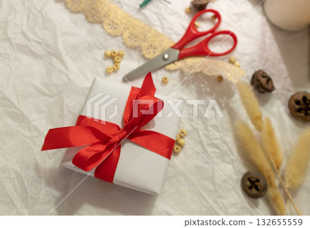 A top view of a Christmas gift wrapped in white paper and tied with ribbon. Scissors and other craft supplies 132655559