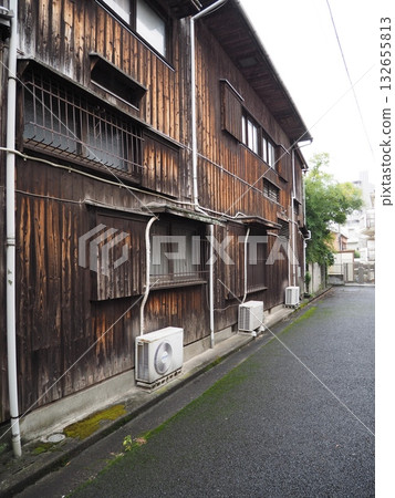 一棟古老的日式房屋，外牆是深色的木質結構，旁邊是一條鋪著濕瀝青的狹窄巷道。 132655813