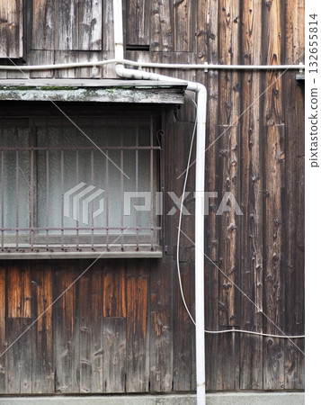 Close-up of the textured wooden exterior wall of an old house and a window with rusty grilles 132655814